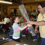 A girl receives a wrapped bouquet from a man at an indoor event.