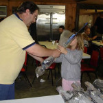 A man and a child exchange wrapped gifts at a gathering.