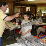 Man demonstrating model airplanes to a boy in a room.
