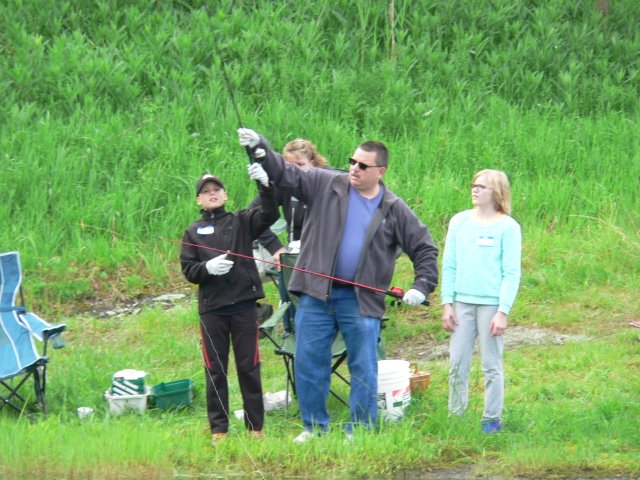 A man and two women standing in the grass holding fishing rods.