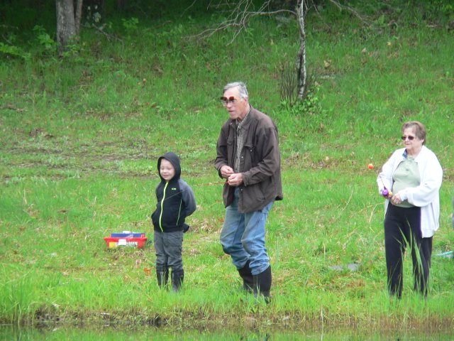 A man and two children fishing in the grass.