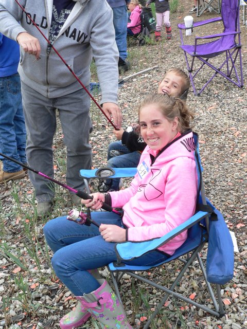A girl sitting in a folding chair holding onto fishing rods.