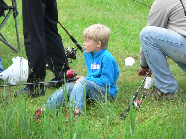 A young boy sitting in the grass with fishing rods.