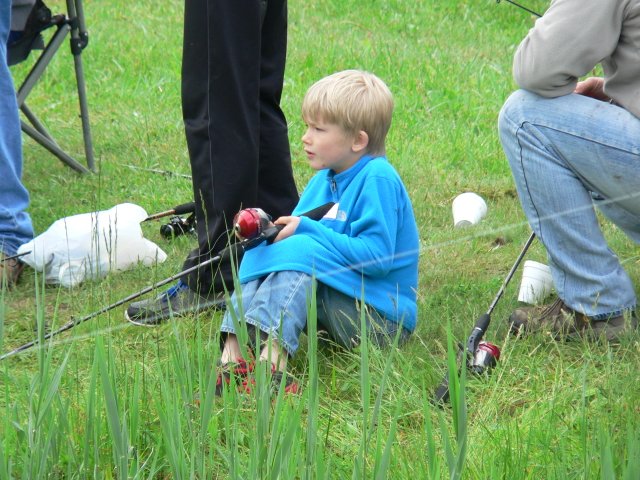 A young boy sitting in the grass holding fishing rods.