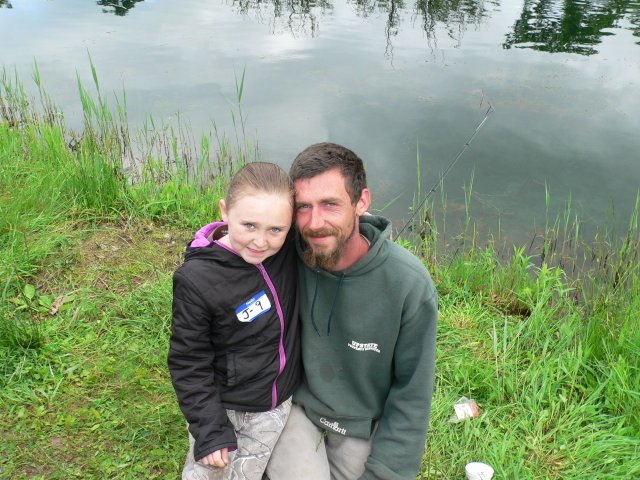 A man and girl posing for the camera near water.
