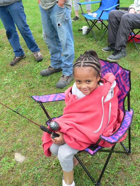A little girl sitting in a folding chair holding onto a fishing pole.