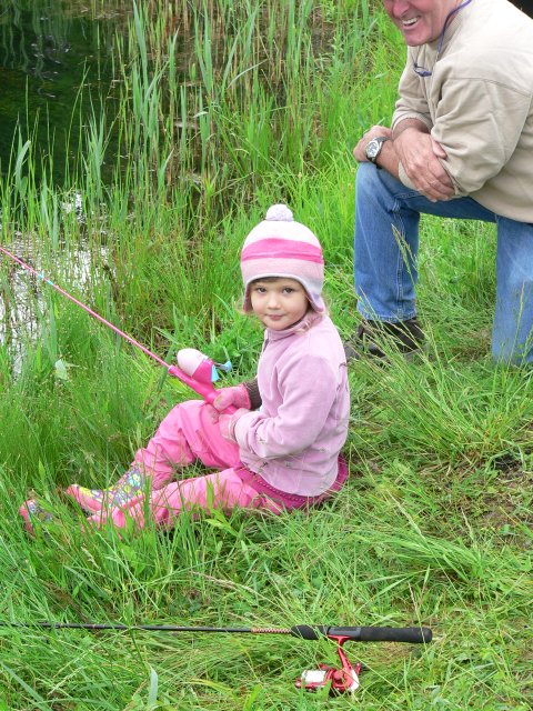 A little girl sitting in the grass with her fishing rod.