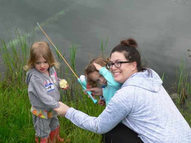 A woman holding onto a fishing pole while two children look on.