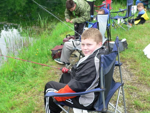 A boy sitting in a folding chair on the grass.