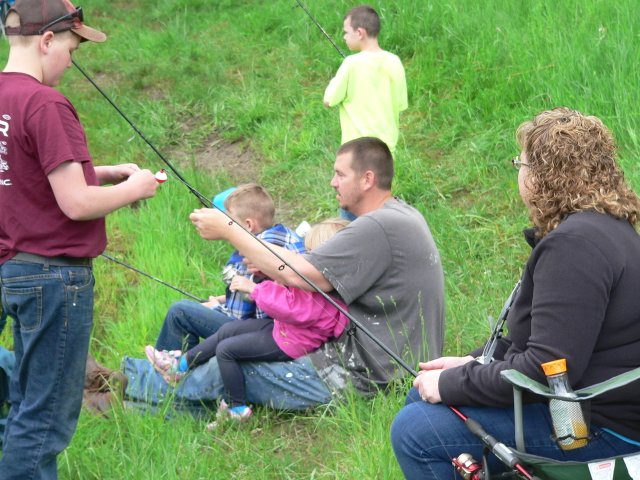 A group of people sitting in the grass holding fishing rods.
