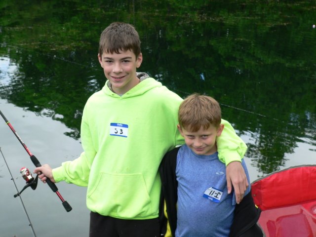 Two boys are standing by a lake holding fishing rods.