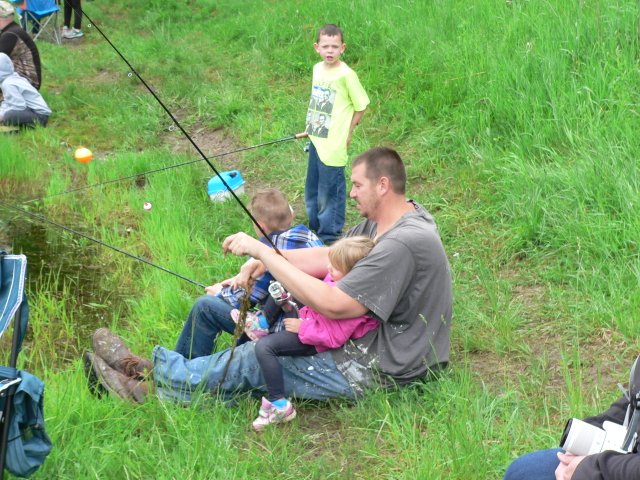A man and two children fishing in the grass.