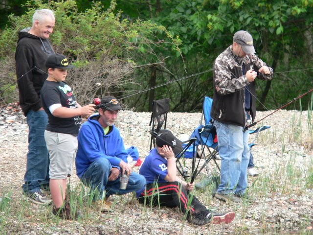 A group of people sitting on the ground with fishing rods.