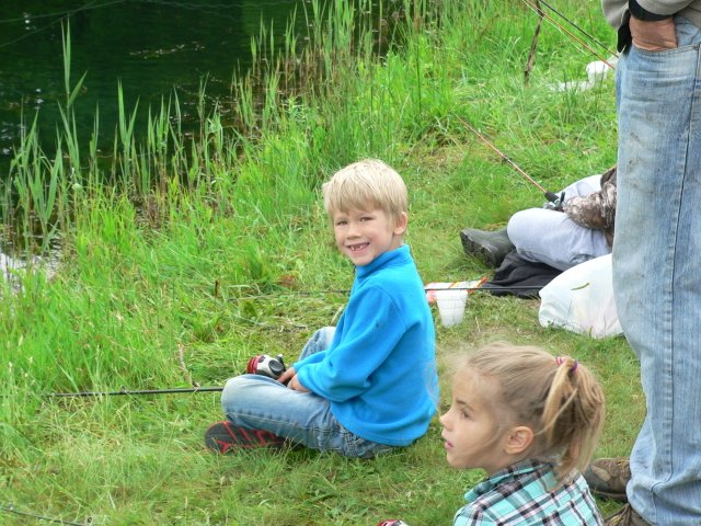 A boy and girl sitting in the grass with fishing rods.