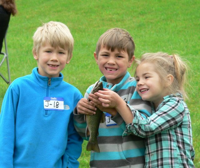 Three children holding a fish in their hands.