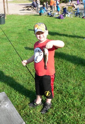 A young boy holding a fish while standing in the grass.