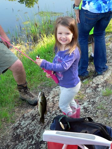 A little girl holding a fish while standing next to some people.