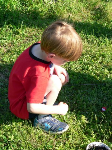A young boy sitting in the grass with his hands on his knees.