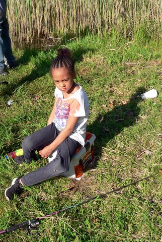A young girl sitting on the ground in grass.