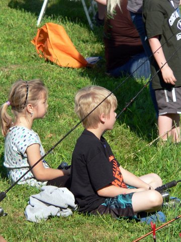 Two children sitting on the grass holding fishing rods.