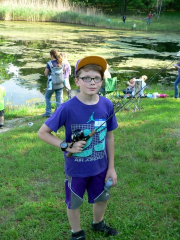 A boy in blue shirt holding a camera near body of water.