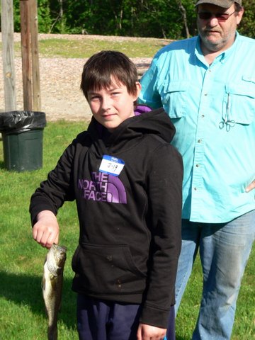 A boy holding a fish while standing next to another man.