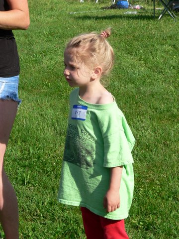A little girl in green shirt standing on grass.